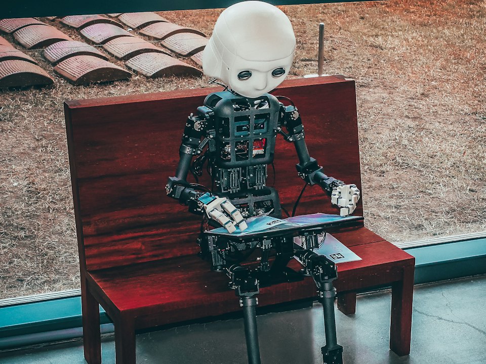 A humanoid robot sitting on a red bench, reading